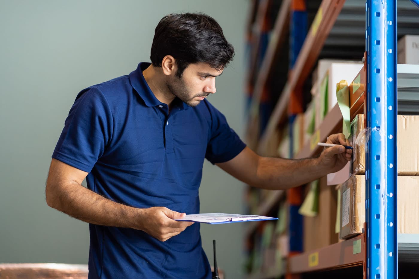 A man in a warehouse inspects items on a clipboard, ensuring everything is in order.