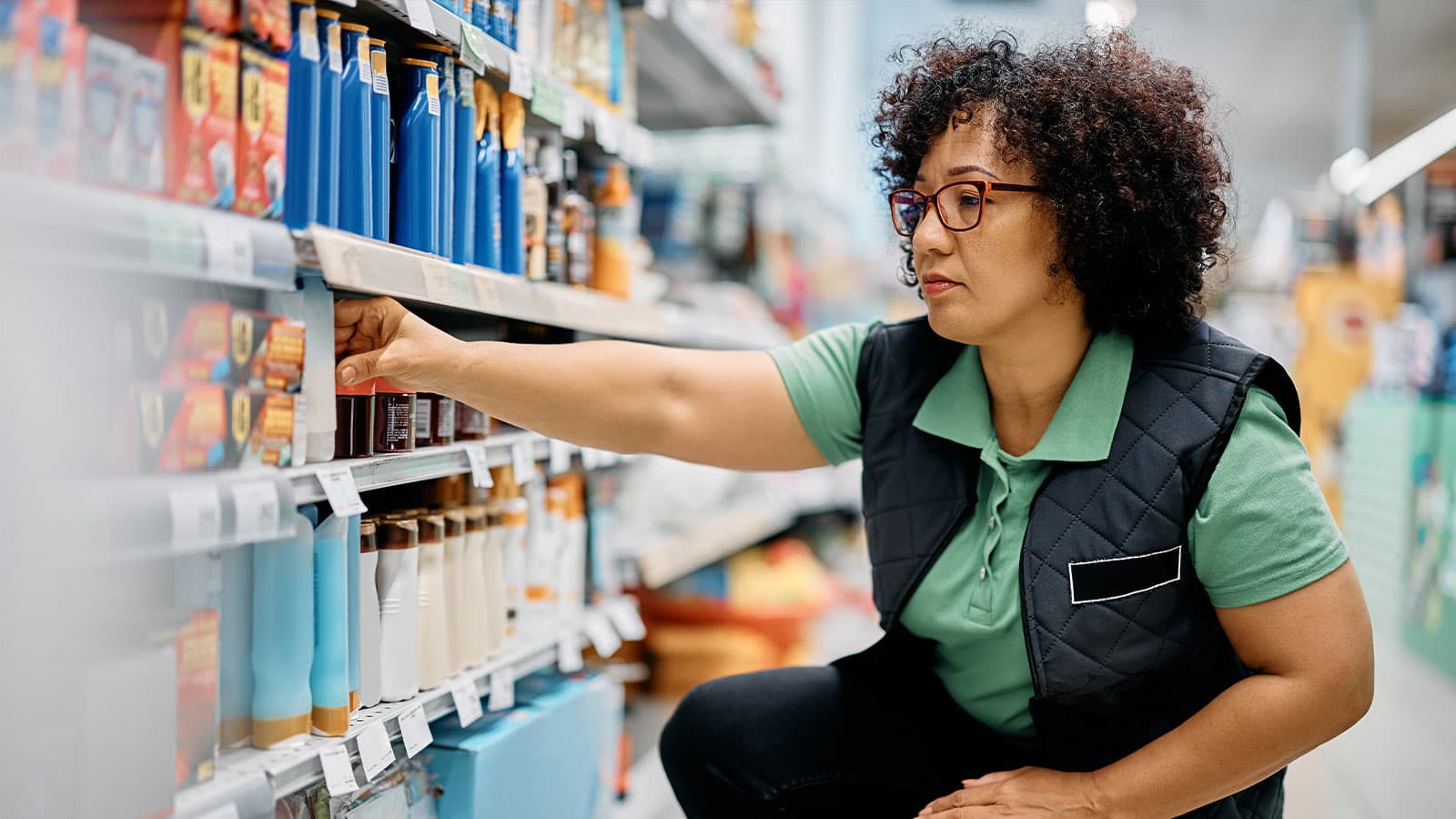 A woman in a store reaching for a product on a shelf.
